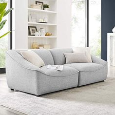 a large gray couch sitting on top of a white rug next to a book shelf