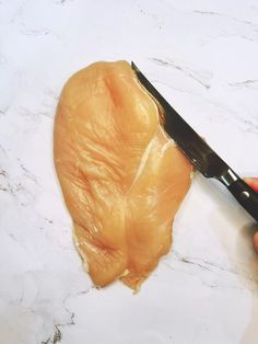 a person holding a large knife over a piece of meat on a counter top with marble