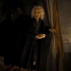 a man with white hair standing next to a curtain in a dark room and smiling at the camera