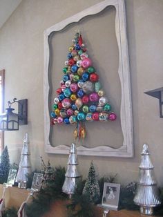 a christmas tree made out of ornaments is displayed in front of a framed photo on the wall