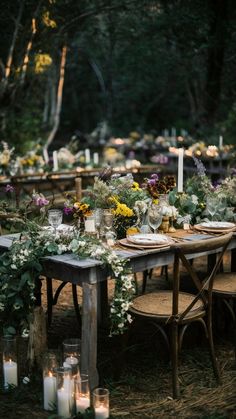 an outdoor dinner table set up with candles and flowers on the table, surrounded by greenery