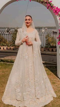 a woman in a wedding gown standing under an arch with flowers on it and wearing a veil