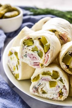 there is a plate that has several wraps on it and two bowls with pickles in the background