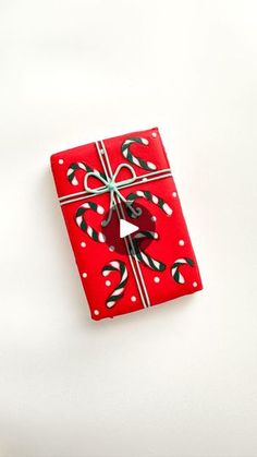 a red gift box with a bow and candy canes on the top is sitting on a white surface