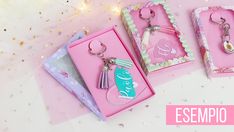 three different key chains in pink boxes on a white table with confetti and stars