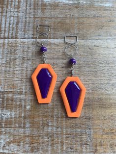 Orange coffin earrings! Handmade with clay. The outer coffins are matte finish, inner purple surface is sealed with resin. Silver tone posts, nickel free. Sealed on the backside to secure loop to hang. Regular Earrings- 3.5 inches long. Tunnel Earrings- 4 inches long.  Clip On Earrings- 3.5 inches long. measurements are approximate.  Jewelry Care: to keep your jewelry in optimal condition avoid dropping them on a hard surface as this can cause chips or fractures of the polymer clay. Keep your jewelry in a dry box or container when not in use. Avoid direct contact of perfumes, lotions or cosmetics while wearing your jewelry. Coffin Vampire, Tunnel Earrings, Coffin Halloween, Coffin Earrings, Gauge Earrings, Halloween Coffin, Ear Hangers, Ear Weights, Gauged Earrings