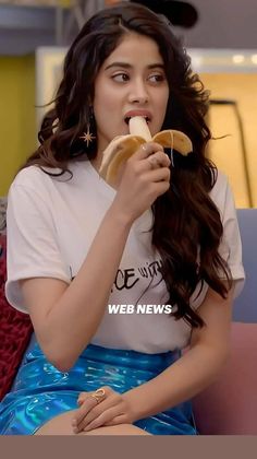 a young woman eating a banana while sitting on top of a pink couch in front of a yellow wall