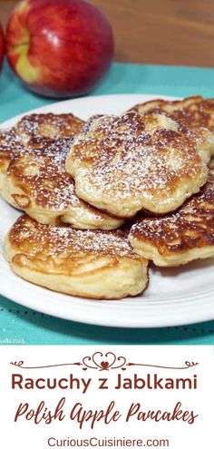 pancakes with powdered sugar on top and apples in the background, sitting on a white plate