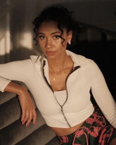 a woman sitting on top of a couch wearing a white shirt and colorful skirt with her hands on her hips