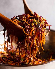 a wooden spoon full of shredded carrots and other foodstuffs in a metal bowl