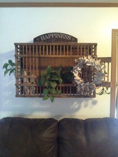 a brown couch sitting next to a wooden wall shelf filled with plants and greenery