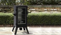 a black wine cooler sitting on top of a stone floor next to a green hedge