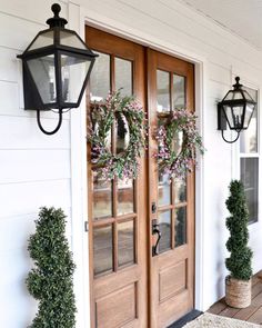 two wreaths on the front door of a house with lanterns hanging from it's sides