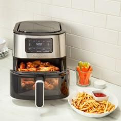 an air fryer with chicken and french fries in front of it on a kitchen counter