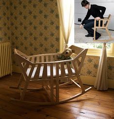 a man kneeling down next to a wooden rocking chair with a dog in the seat