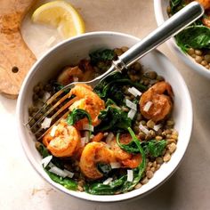 two white bowls filled with shrimp, spinach and lentils next to lemon wedges