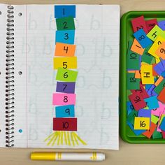 an open notebook with numbers and letters on it next to a green tray filled with colored paper