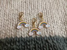 three charms with cats and rainbows on them sitting on top of a knitted blanket