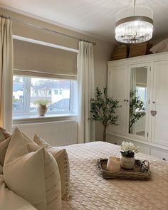 a bedroom with a large bed and white curtains on the window sill, next to a potted plant