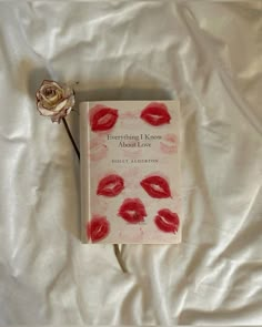 there is a book with red lips and a rose on the white bed sheet next to it