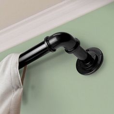 a black pipe on the side of a green wall next to a white towel rack