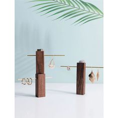 three wooden jewelry stands with earrings on them and a palm leaf in the back ground