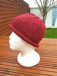 a white mannequin head wearing a red knitted hat on top of a wooden table