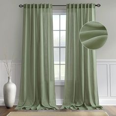 a green curtain hanging in front of a window with a vase on the floor next to it