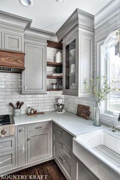 a kitchen with gray cabinets and white counter tops is pictured in this image, there are plants on the window sill