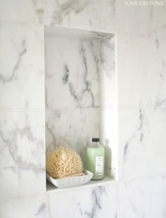 a bathroom with white marble walls and shelves holding soap, shampoo, and other items