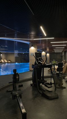 an indoor gym with treadmills, exercise bikes and swimming pool in the background