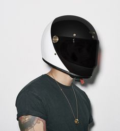 a man wearing a white and black helmet is standing against a gray wall with tattoos on his arm