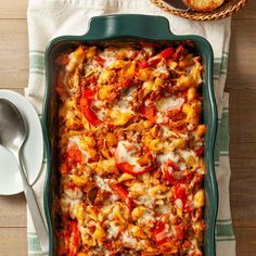 a green casserole dish filled with pasta and meat on top of a wooden table