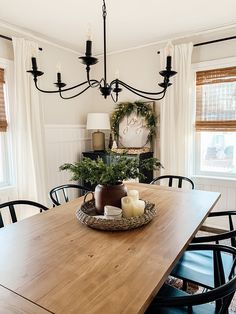 a wooden table with candles on it in front of two windows and a chandelier hanging from the ceiling