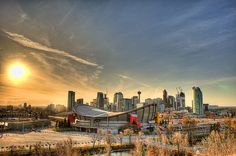 the sun is setting over a city with tall buildings in the foreground and trees on the other side