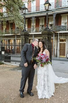 a bride and groom kissing in front of an old building with wrought iron balconies