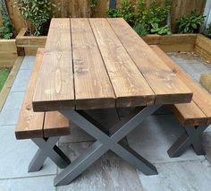 a wooden table sitting on top of a cement floor next to a garden area with potted plants