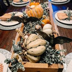 a wooden box filled with pumpkins and greenery on top of a dining room table