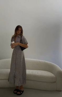 a woman standing in front of a white couch holding a cup and looking at the camera