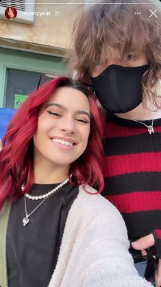 two people with red hair and black face masks are posing for a selfie in front of a building