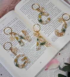 three pieces of jewelry sitting on top of an open book next to flowers and leaves