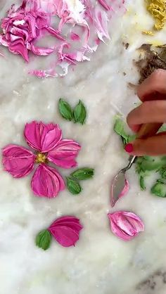 someone is cutting flowers with scissors on a marble counter top that has been decorated with pink and green leaves