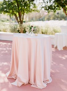 a white table topped with a vase filled with flowers next to two tables covered in pink cloths