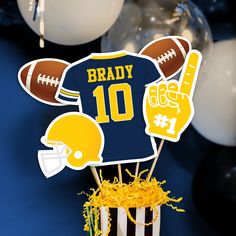 a football themed cake topper sitting in a cupcake holder with yellow streamers