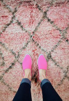 a person wearing pink shoes standing in front of a rug