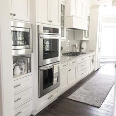 a kitchen with white cabinets and stainless steel ovens, wood flooring and an area rug