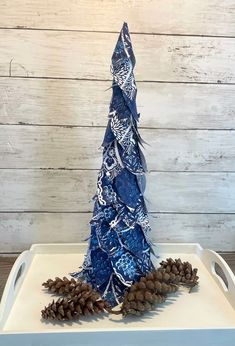 a blue and white christmas tree made out of pine cones on a tray with wood planks