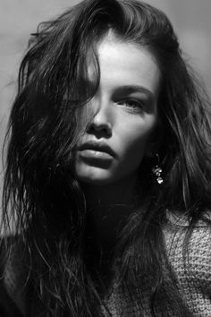 a black and white photo of a woman with her hair blowing in the wind, looking at the camera