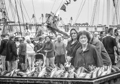 black and white photograph of people standing in front of a boat with fish on it