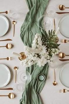 the table is set with white flowers and green napkins, gold cutlery, and silverware